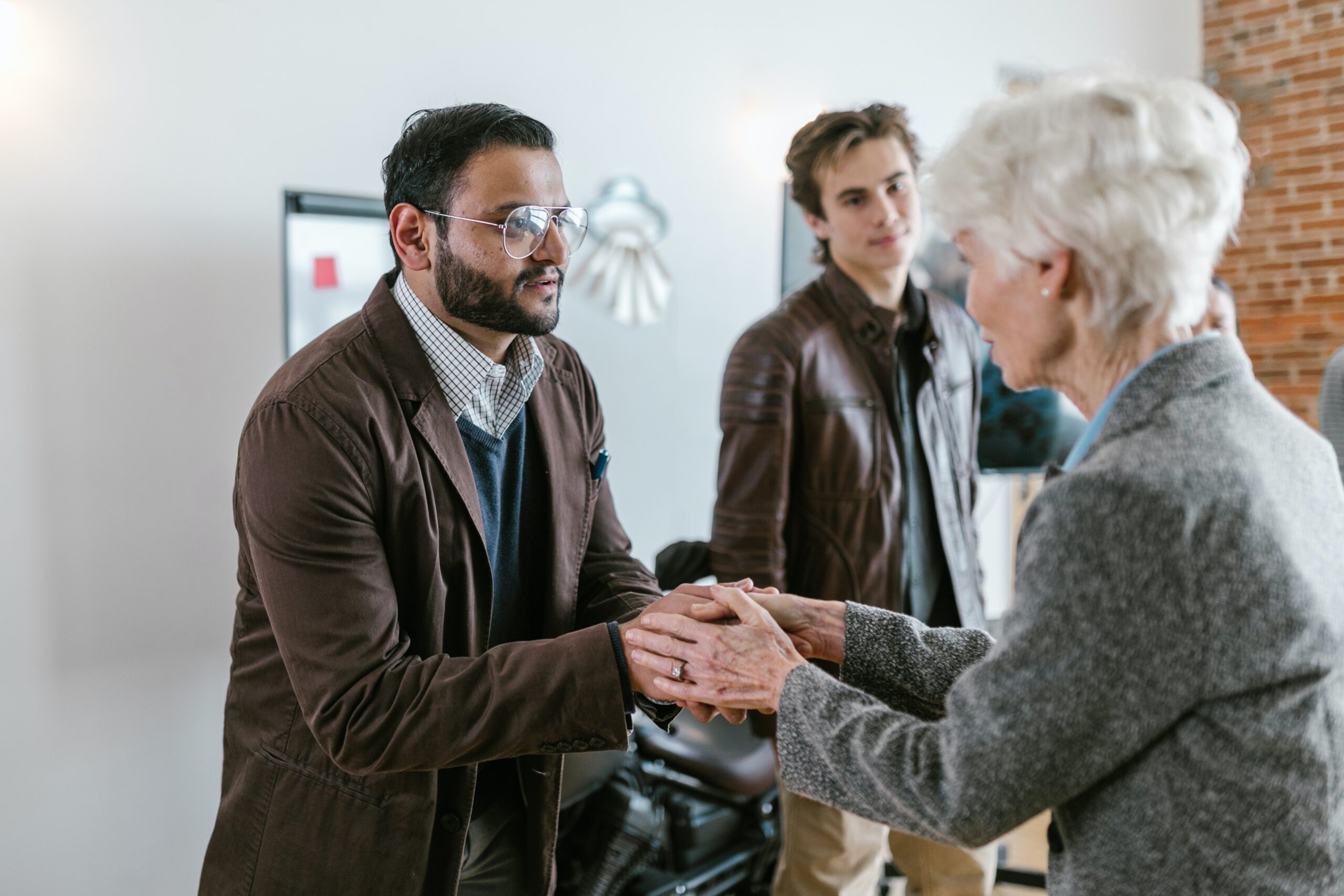 An elderly women who is holding hands with a younger man dressed in a shirt and jacket as she is graciously thanking him.