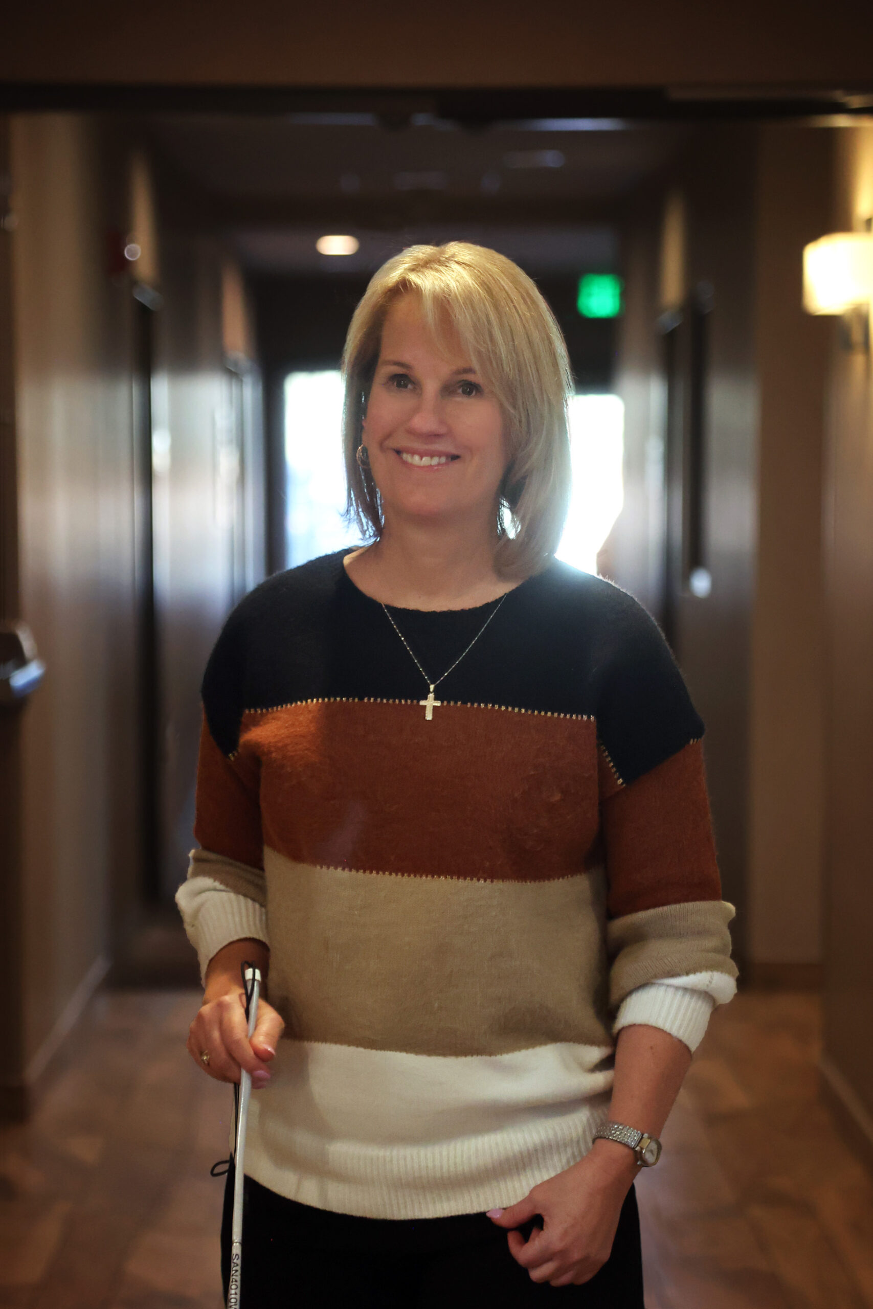 Photo of Suzanne Allee standing in the hallway with a cane in her right hand.