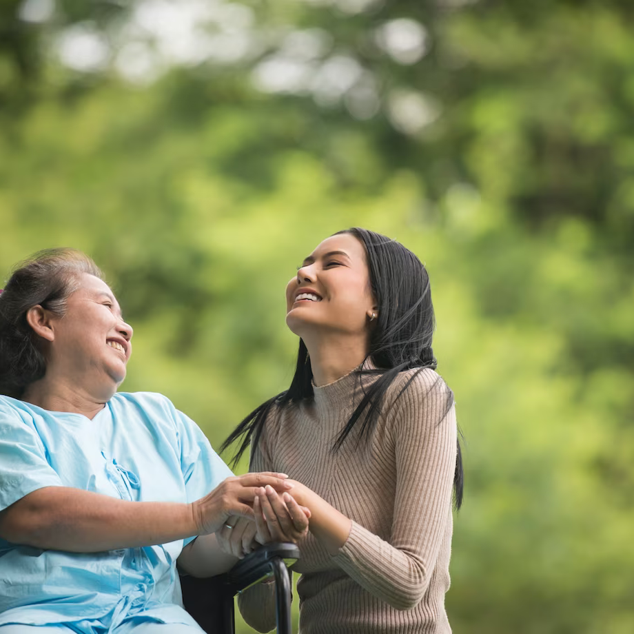 A mom sitting in her wheelchair and clasping hands with her daughter while laughing together