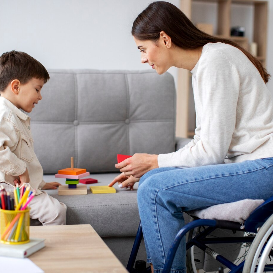 Mon seated in her wheelchair while she plays and works with her son who is seated on the coach.