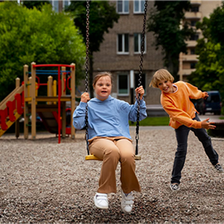 Two children on the playground with one on a swing and the other playfully watching.