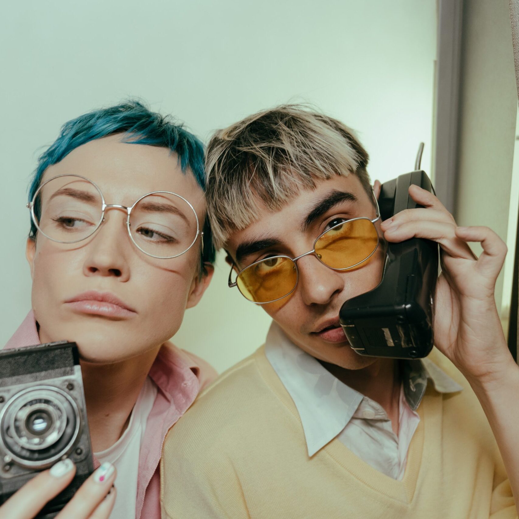 Two people pretending and posing as if they are talking on an old cell phone and using a 35mm camera.