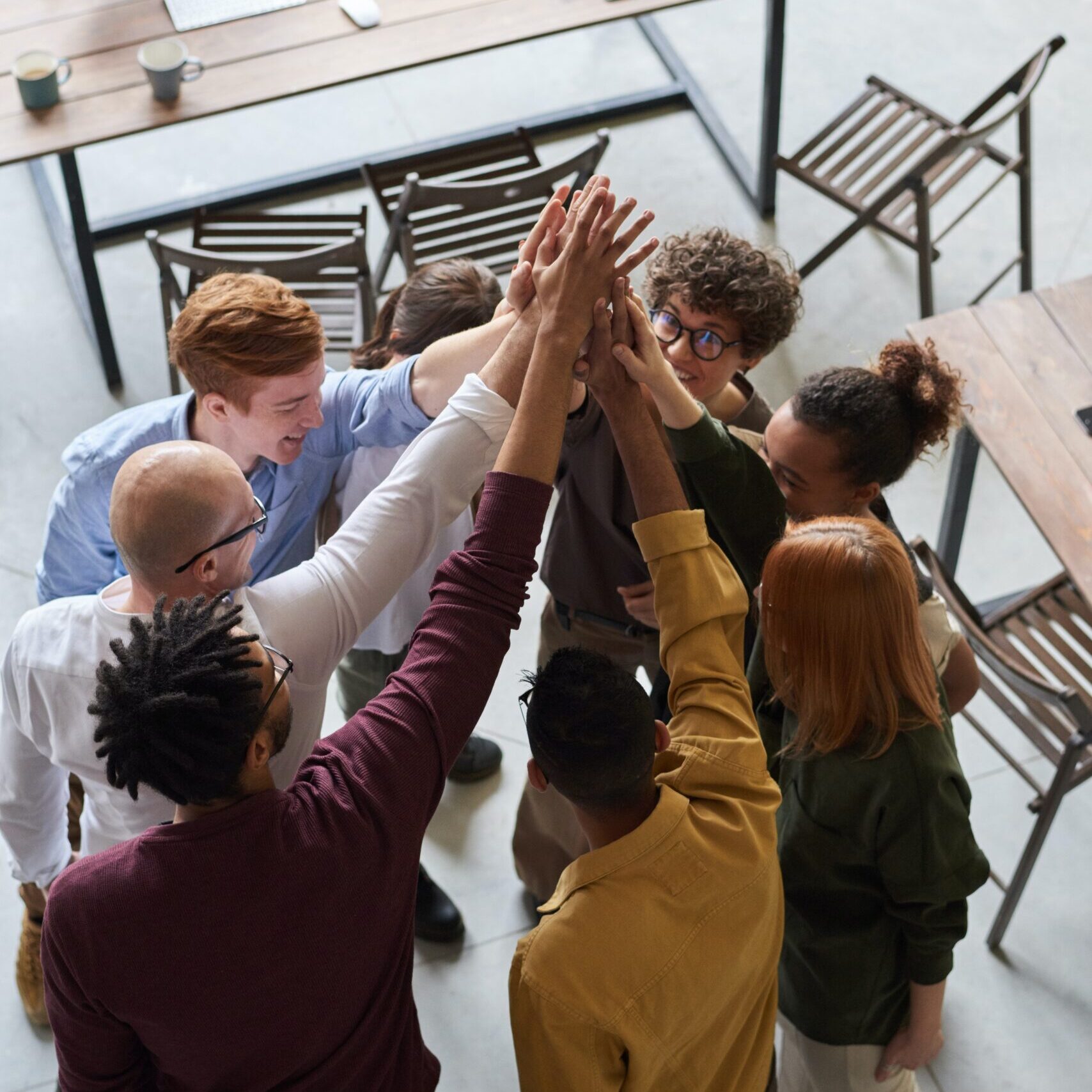 Four happy group of eight young adults having fun and high giving a high five to each other together while celebrating an accomplishment.